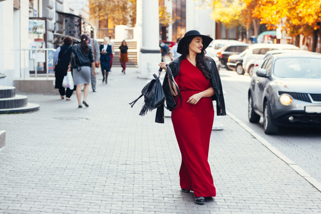 63834524 - young stylish woman wearing red maxi dress, black leather jacket and hat walking on the city street in autumn. fall fashion, elegant look. plus size model.
