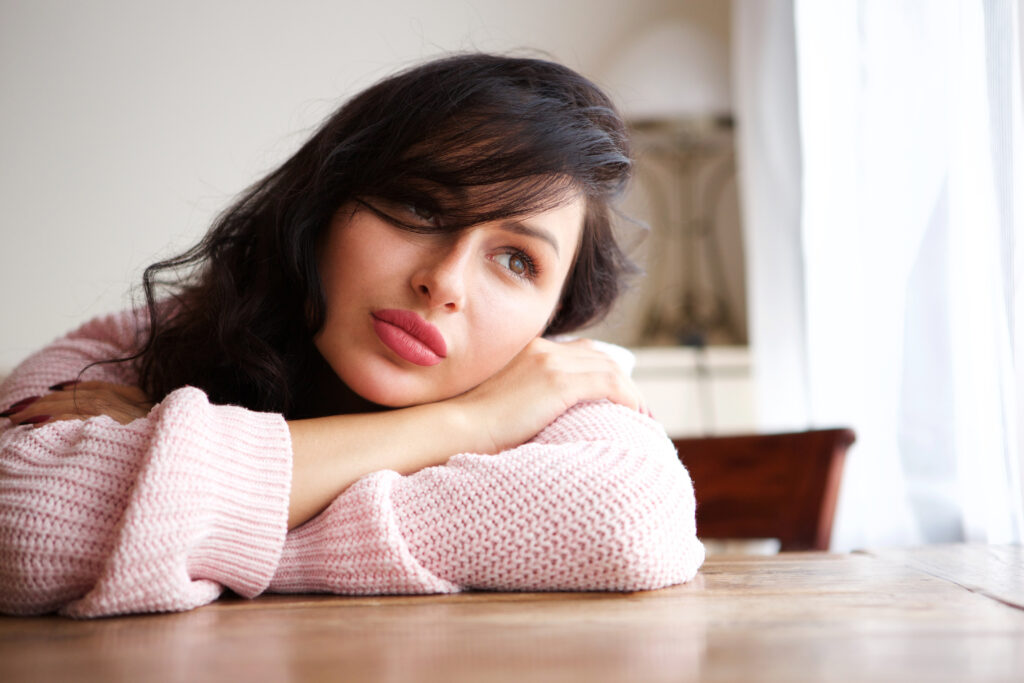 Close up portrait of sad woman in contemplation sitting and leaning on table